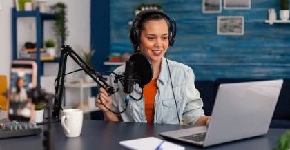 Eine junge Frau sitzt am Notebook vor einem Mikrophon. Sie nimmt einen IT-Podcast auf.