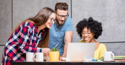 Ein junges dynamisches Team steht zusammen im Büro. Sie blicken auf den Bildschirm eines Notebooks und reden über CMS Hosting.